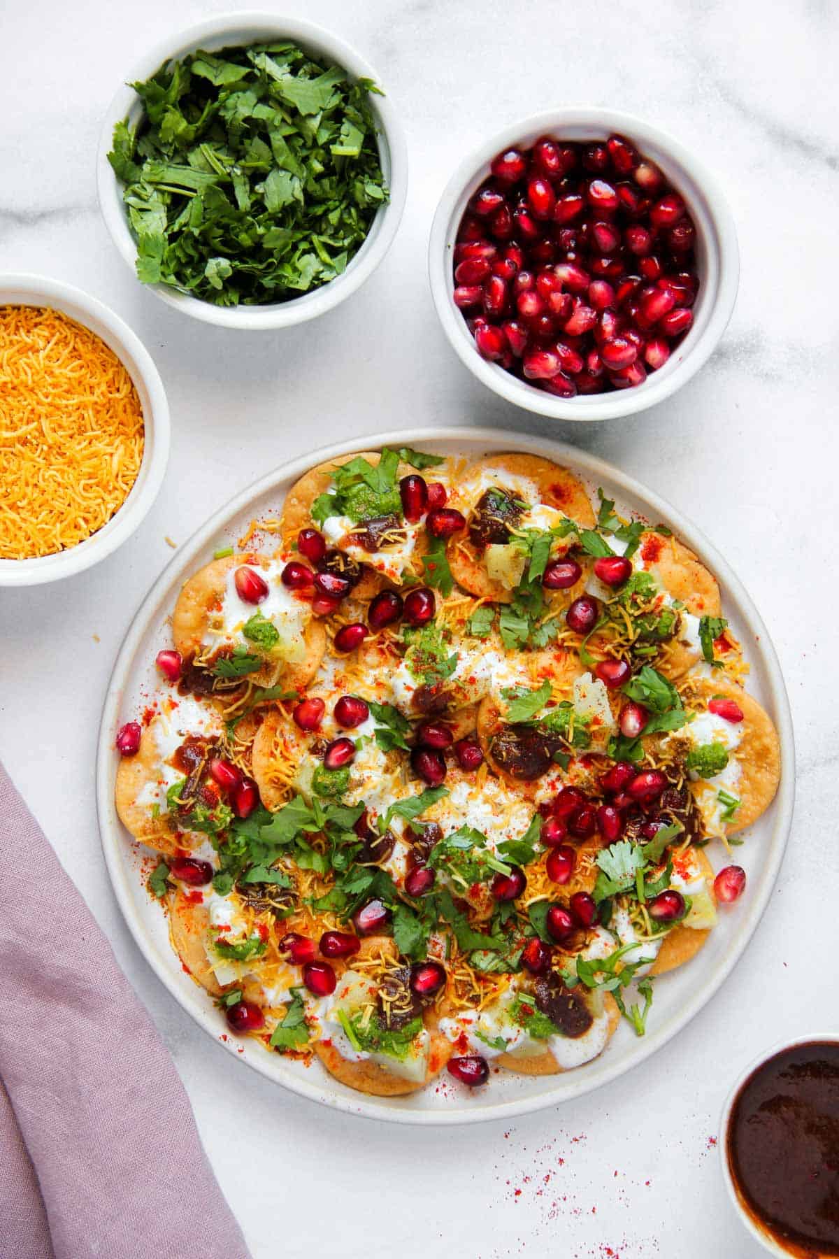 Papdi chaat served in a white platter with garnishes on the side in small bowls.