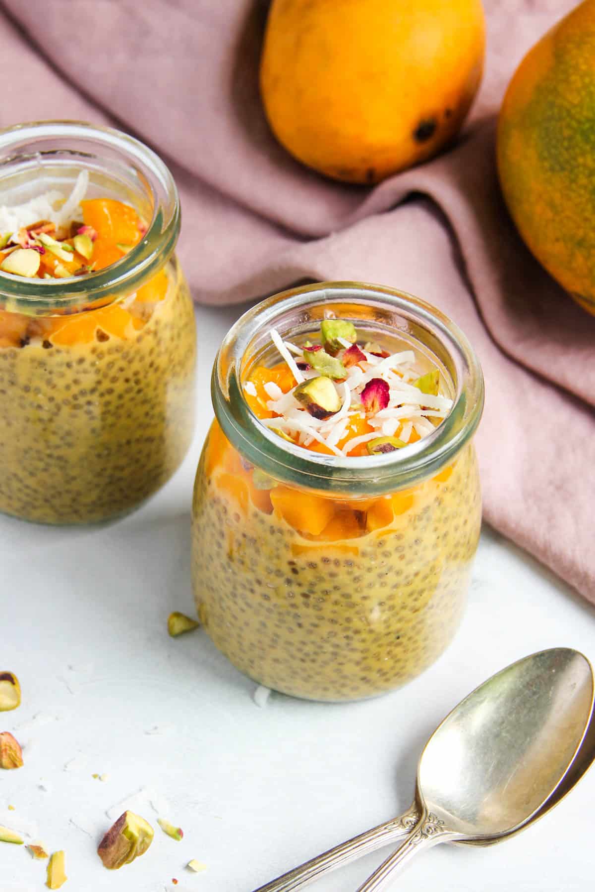 Mango chia pudding in a two glass jars garnished with diced mango, coconut and pistachios 