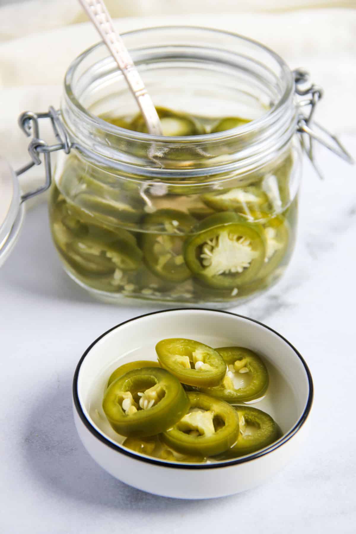 pickled jalapeños in a glass jar and a small white dish