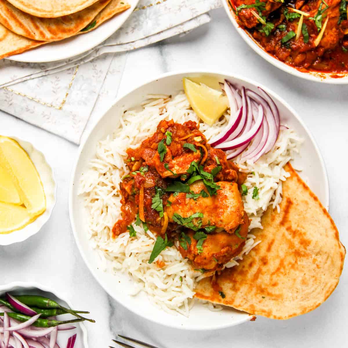 karahi chicken served over basmati rice along with naan, sliced onions and lemon wedge