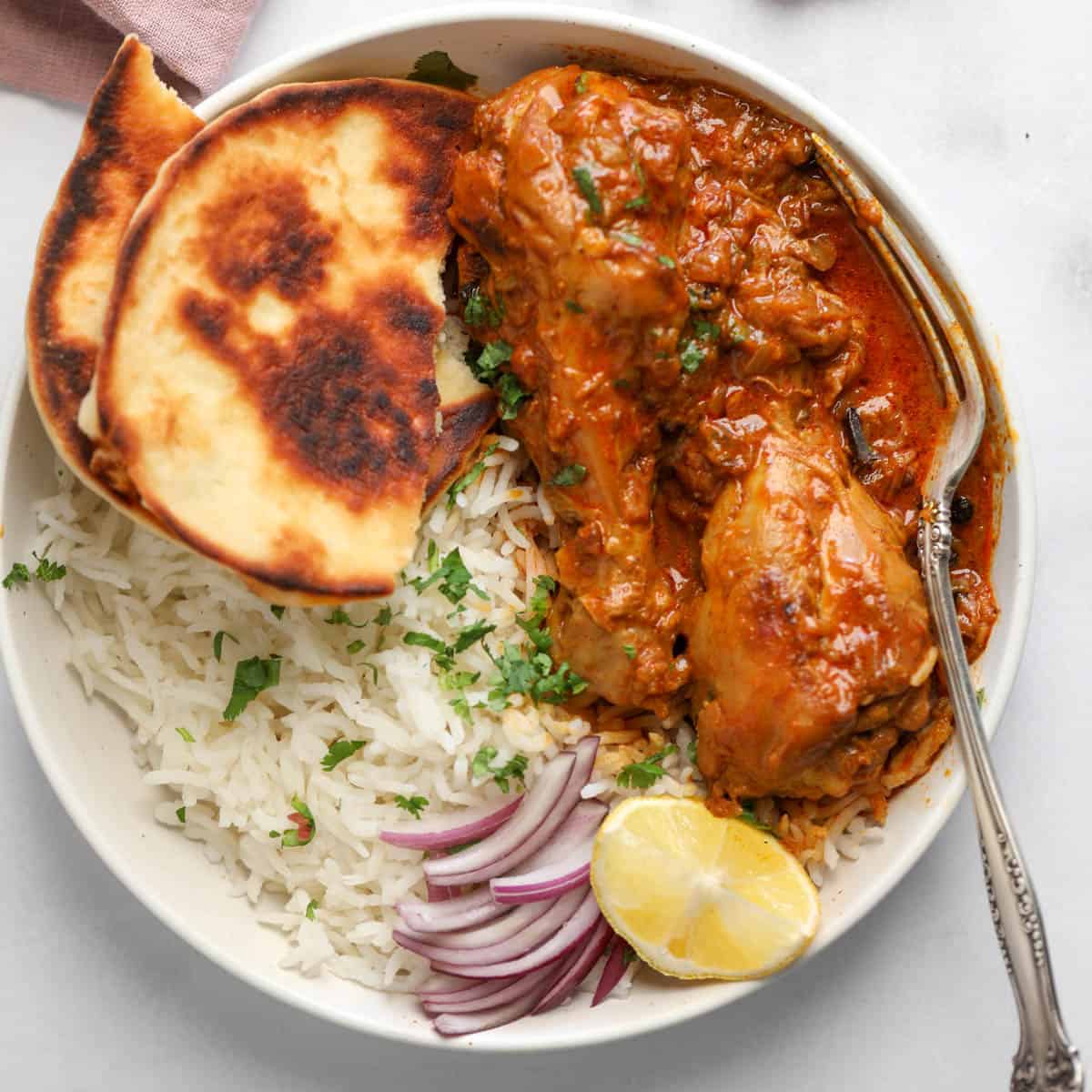 chicken korma in s white bowl with rice and naan