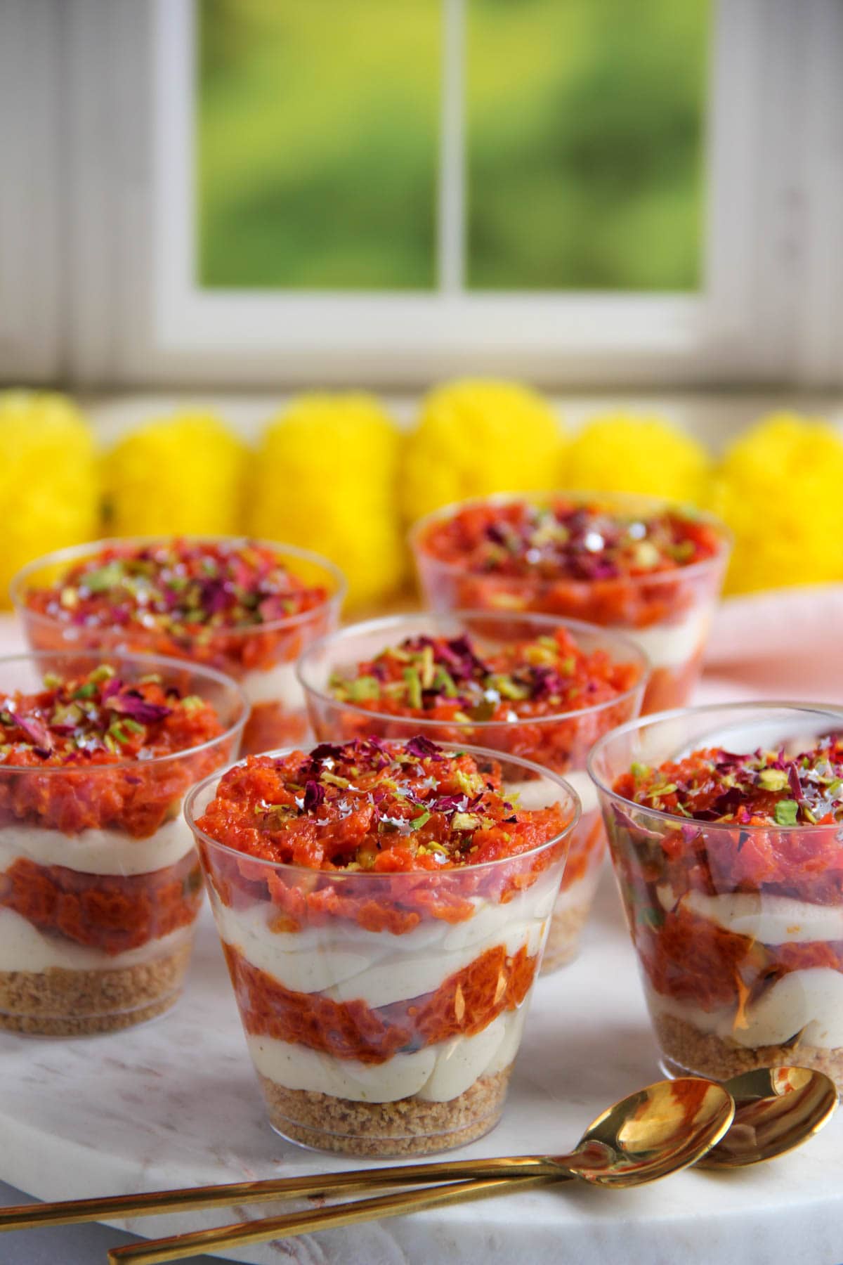 carrot halwa cheesecake jars garnished with pistachios and rose petals.