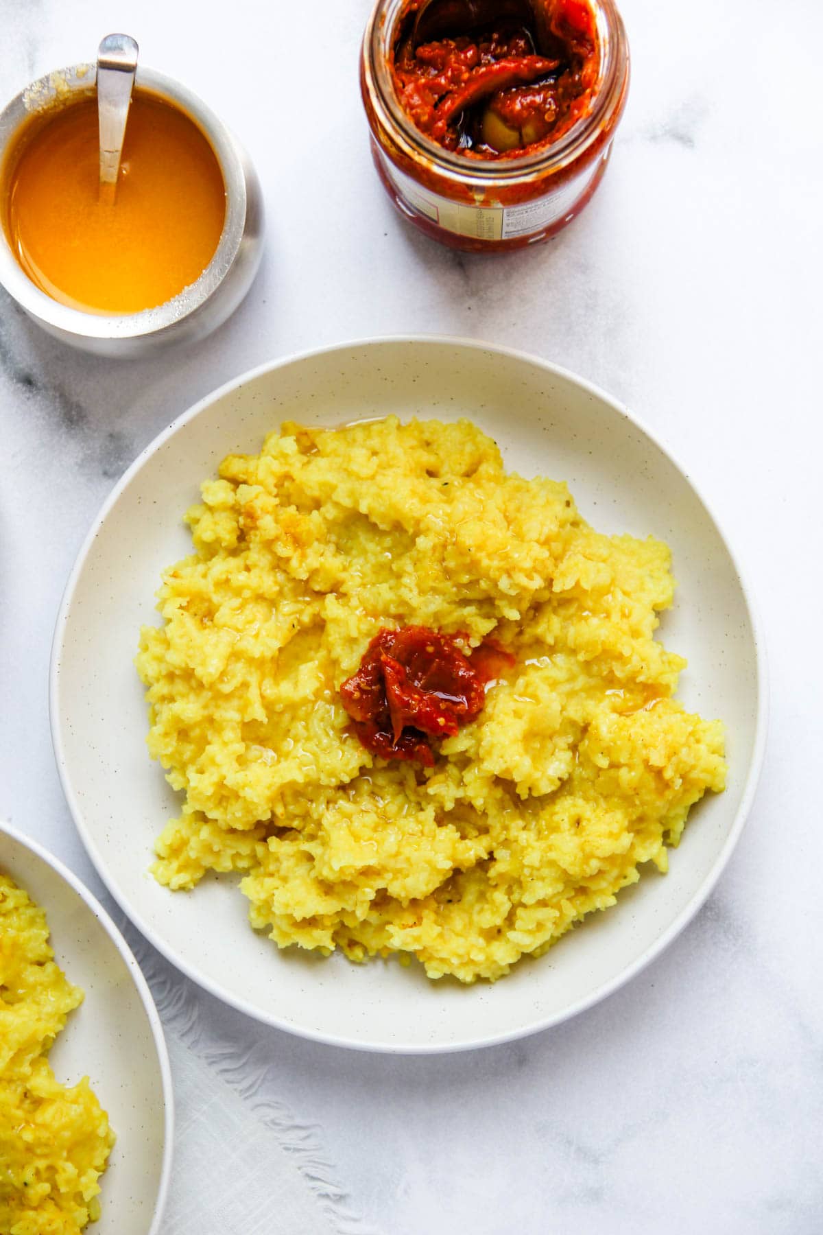 Khichdi served in a white bowl with pickle and ghee. 